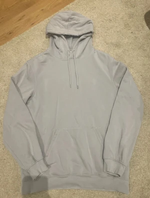 Ljusblå hoodie från H&M Divided - Säljer en enkel och stilren ljusblå hoodie från H&M Divided i storlek S. Tröjan har huva med snörning, magficka och mjukt fleecefoder på insidan. Perfekt för chill dagar och när du vill ha något bekvämt och snyggt.