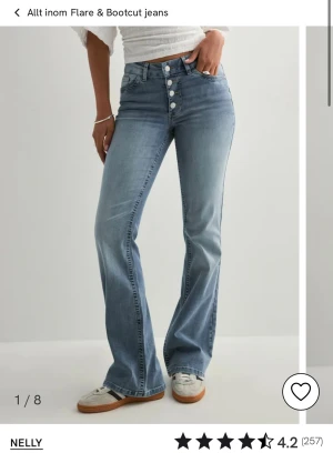 Bootcut jeans med knappar från Nelly - Snygga ljusblå bootcut jeans från Nelly med mellan hög midja och flera framträdande knappar framtill. Jeansen har klassisk femficksdesign och är tillverkade i mjukt denimtyg som sitter skönt. Perfekt för dig som gillar retrovibbar och en avslappnad look.