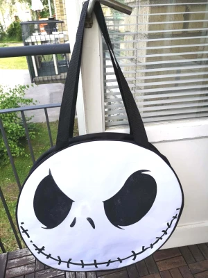 Jack Skellington axelväska - Mått:54*50*15cm, helt ny. Stor rund axelväska med Jack Skellingtons ansikte från Nightmare Before Christmas. Väskan är svart och vit med 2st breda axelremmar(Längd 80cm,ej justerbar). Perfekt för dig som älskar unika accessoarer och vill sticka ut med en cool och lekfull design, vattentätt material.