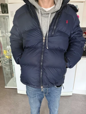Mörkblå dunjacka från Polo Ralph Lauren - Snygg mörkblå dunjacka från Polo Ralph Lauren med röd logga på bröstet, säljer den eftersom jag köpt ny jacka. Riktigt skön och varm nu inför vintern, nypris cirka 6000