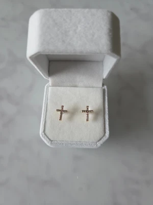 Örhängen med kors - Snygga örhängen i form av kors med glittrande stenar, infattade i en guldfärgad metall. Perfekt för dig som gillar detaljer som sticker ut och vill ha något som känns både trendigt och personligt.