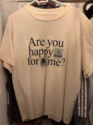 The Big Steppers Tour '22 t-shirt - Sällsynt Beige Kendrick Lamar t-shirt med tryck fram och bak från The Big Steppers Tour '22. Framsidan har texten 'Are you happy for me?’