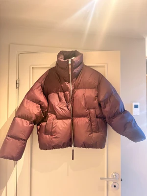 Vinröd pufferjacka Second Female - Säljer en  pufferjacka från Second Female i storlek M. Jackan har hög krage, två sidofickor och grov dragkedja framtill. Den är oversized och har långa ärmar, perfekt för kalla dagar. Ny pris 2500kr