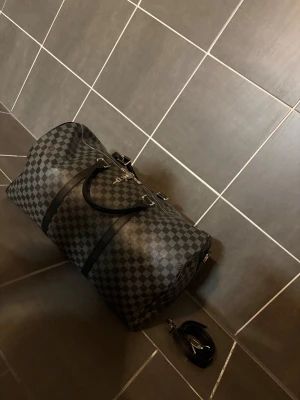 Louis Vuitton damier graphite kepall/ resväska i skinn - Snygg och rymlig resväska från Louis Vuitton i klassiskt rutigt mönster. Louis Vuitton damier graphite kepall/ resväska i skinn. Väskan är svart och grå med detaljer i skinn, silverfärgad dragkedja och lås med nycklar. Medföljer avtagbar axelrem för extra flexibilitet.