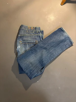 Dondup blå jeans, storlek 33 - Snygga blå jeans från Stan Dart, tillverkade i Italien. Modellen har klassisk femficksdesign, gul kontrastsöm och lätt slitna detaljer framtill för en cool look. Jeansen är raka i benen och gjorda i 100% bomull för skön känsla.