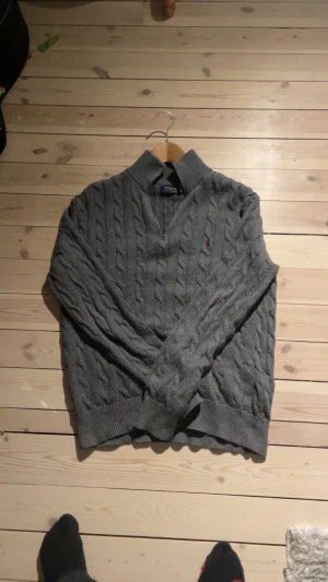 Grå kabelstickad tröja Polo Ralph Lauren - Säljer en grå kabelstickad tröja från Polo Ralph Lauren med halv dragkedja och v-ringad krage. Tröjan har långa ärmar och klassisk broderad logga på bröstet. Perfekt för lager-på-lager och chill stil. Storlek S. Hör av dig vid frågor!                                                                    Byten kan vara intressant 