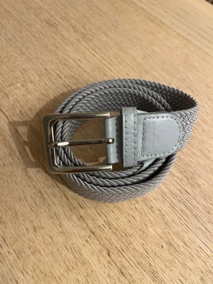 Grått flätat bälte - Fräscht grått flätat bälte som både lyfter outfiten och byxorna, 110 cm (elastiskt). Små tecken på användning. Tveka inte att höra av dig med funderingar!