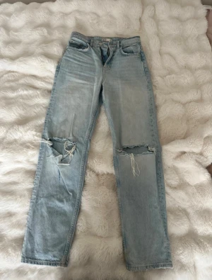 Ljusblå ripped jeans  - Säljer ett par ljusblå jeans från Gina  med raka ben och snygga slitningar över knäna. Klassisk femficksmodell med dragkedja och knapp. Perfekt för dig som gillar en avslappnad och trendig look.
