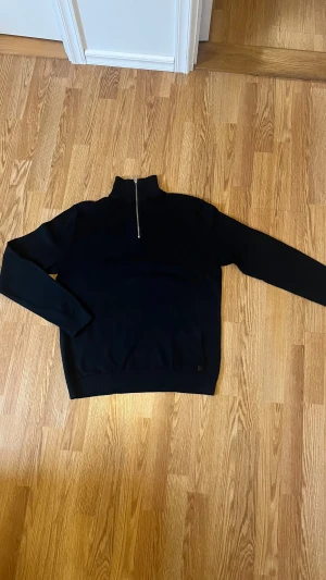 Svart half zip tröja Jack & Jones - Svart långärmad tröja från Jack & Jones med half zip och hög krage. Tröjan har en diskret textur på övre delen och är gjord i mjuk bomull. Perfekt för dig som gillar stilrena och enkla plagg med en modern touch.