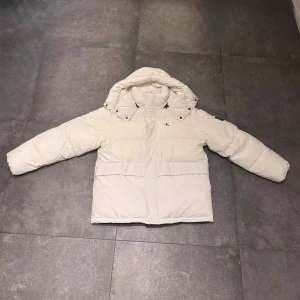 Vit pufferjacka från Calvin Klein Jeans - Säljer en clean vit pufferjacka från Calvin Klein Jeans med avtagbar huva och snygg CK-logga på ärmen. Jackan har dragkedja och knappar framtill, två stora fickor och är riktigt fluffig. Perfekt för kalla dagar när du vill hålla dig varm och stilig. Jackan är endast använd 1 gång och säljer den då jag tyckte jackan var för stor för mig.