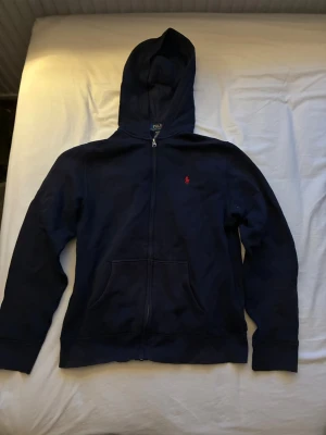 Blå ralph lauren zip hoodie - En mörkblå Ralph lauren ziphoodie. Storlek S passar xs. Tröjan är använd rätt så mycket men den år i väldigt bra skick fortfarande.