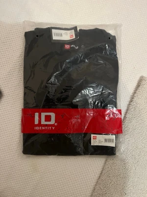 Svart t-shirt från ID Identity - En klassisk svart t-shirt från ID Identity. Enkel och stilren design utan mönster, perfekt till alla outfits. Tillverkad i mjuk bomull för skön känsla hela dagen. T-shirten har normal passform och korta ärmar.