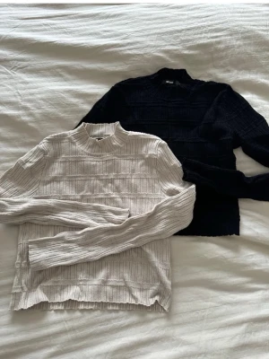 Ribbad långärmad tröja från Bik Bok - Två ribbade långärmade tröjor från Bik Bok, en i svart och en i ljusbeige. Båda har hög krage och ett snyggt strukturerat mönster med horisontella ränder. Perfekt att styla med jeans eller kjol för en chill look.