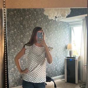 Vit prickig blus med volangärmar - Supersöt vit blus med svarta prickar och volangärmar. (Pris kan diskuteras) Säljer för att jag inte har någon användning av den. Har använt typ 4 ggr🩷🩷köpt på plick så det är inte mina bilder utan hon som jag köpte av har tagit bilderna 🙌