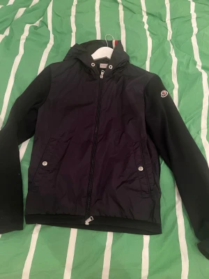 Moncler vindjacka S - Säljer en vindjacka från Moncler. Framsidan och luvan är i samma material som en windbreaker medans armarna och baksidan är som en cardigan. Den är i bra skick, dock har snörena i luvan gått bort. Nypris: 6799kr. Kvitto finns.