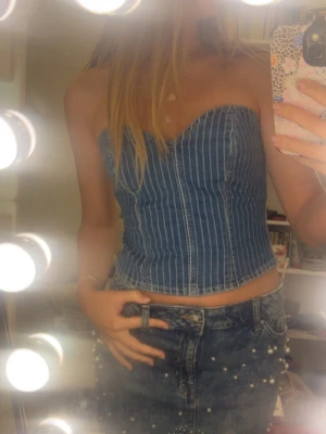 Denim korsett-topp - Säljer en snygg korsett-topp i denim med vertikala vita ränder. Toppen är axelbandslös och har en bandeauformad siluett som ger en jätte fin utseende. Köpt för 400kr 🤗 
