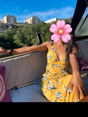 Gul blommig långklänning med v-ringning - Säljer en superfin gul långklänning med blommigt mönster och v-ringad front. Klänningen har smala axelband och ett omlottliknande liv. Perfekt för soliga dagar och har en flowy, avslappnad passform. Materialet känns lätt och luftigt. Den har även öppen rygg med knytning 🥰💛