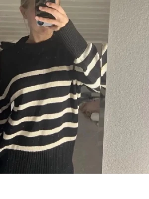 Svartvit randig stickad tröja - Säljer en svart stickad tröja med vita horisontella ränder. Tröjan har en rund hals och långa ärmar med ribbade muddar. Modellen är loose fit och passar perfekt för dig som gillar en avslappnad stil.