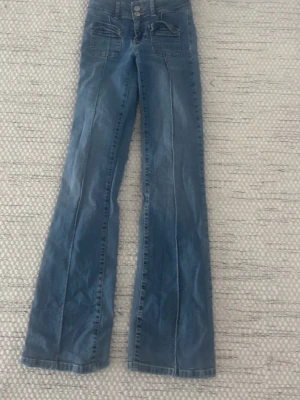 Blå bootcut jeans med fickor - Blåa Nelly jeans utsvängda storlek 32 är mycket använda och har slitage som ni ser på sista bilden annars hur fina som helst. Skriv innan ni köper 