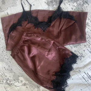 Vinröd satinlinnetopp med spetsdetaljer - Säljer en vinröd linnetopp i satin med svarta spetsdetaljer längs urringningen och nederkanten. Perfekt pyjamas sett. Tunt axelband och glansigt material.