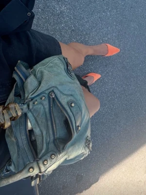 Blå Balenciaga axelväska i skinn - Säljer en blå väska från Balenciaga i mjukt skinn med snygga guldfärgade detaljer och dragkedjor. Modellen är city first! Längden är 34cm och bredd 6cm. Perfekt storlek för allt du behöver ha med dig.köpt för 12 000kr på collector’s cage och därmed medföljer äktenskapet från deras egna ”undersökningar”! Självklart medkommer dustbag och äktbeviset! Finns lite slitage på botten av väskan och vid dragkedjans övre kant (allt visas på bilderna)OBS första bilden är inte min, utan används mer för inspo