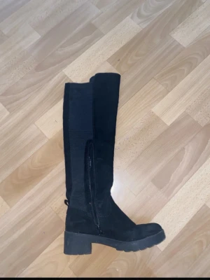 Svarta höga boots med klack - Säljer ett par svarta höga boots i mocka med chunky klack och dragkedja på insidan. Skorna har rund tå och grov sula som ger en cool vibe. Perfekta till höst- och vinteroutfits. Passar dig som gillar stilrena och bekväma skor.