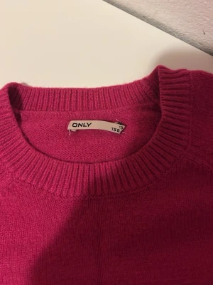 Mörkrosa stickad tröja från ONLY - Säljer en mörkrosa stickad tröja från ONLY med rund hals och ribbade muddar vid ärmslut och nederkant. Tröjan är väldigt skön och mjuk i materialet! Något nopprig men annars i fint skick! 