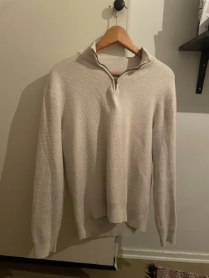 Beige stickad tröja med half zip - Säljer en beige stickad tröja med halv dragkedja i halsen. Tröjan har en diskret struktur, ribbade muddar och lång ärm. Perfekt för lager-på-lager och chill dagar. Enkel att matcha med jeans i både grått och blått. Priser går att diskutera