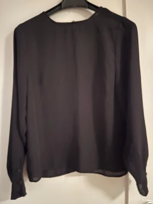 Tunn ”chiffong” blus, svart, Gina Tricot  - Tunn ”chiffong” blus, svart, Gina Tricot. Fina knappdetaljer vid ärmslut, knapp i nacken. Blusen är svart - färgåtergivningen på bilderna är inte är så bra.