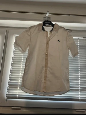 H&M Short Sleeve Button-Up Shirt – White & Beige – Size XS - Stylish short-sleeve button-up shirt from H&M. White base with beige contrast details on the collar and button placket, plus a small embroidered bird logo on the chest. Lightweight and comfortable fabric, perfect for summer, smart-casual outfits, or layering. In good condition with normal signs of wear. Brand: H&M Size: XS (EUR 34 / UK 6 / US 2) Color: White / Beige Sleeve length: Short sleeve Fit: Slim / regular Condition: Good From a smoke-free home. Feel free to message me if you have questio