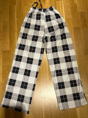 Rutiga pyjamasbyxor  - Vit, svart och grå rutiga pyjamasbyxor i ett silkes liknande material. Storlek XS/S. Raka i benen och knyte i midjan. Säljes då de inte kommer till användning längre. Djur och rökfritt hem. Finns även två fickor på vardera sida.