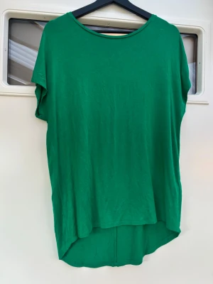 Grön loose topp med rund hals - Säljer en enkel grön topp med rund hals och loose passform. Toppen är ärmlös och har en längre baksida för en chill look. Perfekt till jeans eller shorts när du vill ha något bekvämt och stilrent. Materialet känns mjukt och lätt.