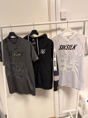 Vit Siksilk t-shirt med tryck - Vit t-shirt från Siksilk med svart och guld logotyp på bröstet och stort 84-tryck framtill. Sportig design med meshpaneler och korta ärmar, samt detaljerade muddar med Siksilk-tryck. Perfekt för dig som gillar streetwear och snygga detaljer.