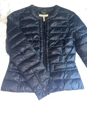 Svart dunjacka med leoparddetaljer - Snygg svart dunjacka  med raka quiltade paneler och dragkedja framtill. Jackan har leopardmönstrade detaljer på insidan av sömmarna som ger en cool kontrast. Materialet är glansigt och känns lätt men ändå varmt. Perfekt för dig som vill sticka ut lite extra.