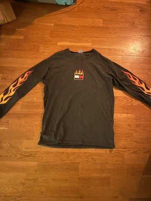 Tommy Hilfiger långärmad t-shirt med flames - Cool svart långärmad t-shirt från Tommy hilfiger med eldflammor i orange och gul längs båda ärmarna. På bröstet finns en liten logga med flames ovanför. Tillverkad i mjuk bomull och har en relaxed fit som passar perfekt till streetwear. Använd 1 gång så i mycket bra skick!