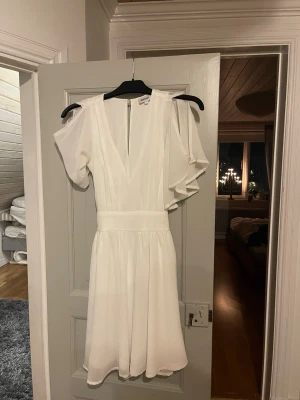 Vit klänning - Supersöt vit kortklänning från Bubbleroom med v-ringad front, omlott-detalj och knytband i midjan. Den är perfekt till student eller konfirmation! Klänningen har luftiga, korta ärmar i ett skirt material som ger en romantisk vibe. Perfekt för sommarens alla tillfällen!