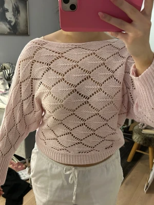 Ljusrosa stickad tröja med hålmönster - Säljer en ljusrosa stickad tröja med snyggt hålmönster i diamantform. Tröjan har lång ärm, bredare halsringning och ribbade muddar. Perfekt för vår eller sommarkvällar när du vill ha något luftigt men ändå mysigt.