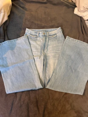 Ljusblå wide jeans från H&M Divided - Säljer ett par ljusblå jeans från H&M Divided i storlek 34. De har hög midja och breda ben för en riktigt chill och trendig look. Klassisk femficksmodell och tillverkade i mjukt bomullsjeans. Perfekta till sneakers eller boots!