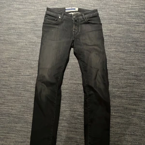 Gråa jeans från Jacob Cohën - Säljer ett par svarta skinny jeans från Jacob Cohën, tillverkade i Italien. Jeansen har klassisk femficksdesign, smal passform och är gjorda i mjukt denimtyg. Snyggt Jacob Cohën-läderpatch bak i midjan och diskreta sömmar för en clean look. Storlek 30/30 (köpta i Italien) har inte kvitto men QR funkar 