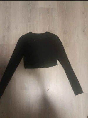 Svart croppad långärmad topp - En enkel och stilren svart croppad topp med långa ärmar. Perfekt att matcha med höga jeans eller kjol för en clean look. Mjuk och stretchig känsla, rund halsringning och figurnära passform.