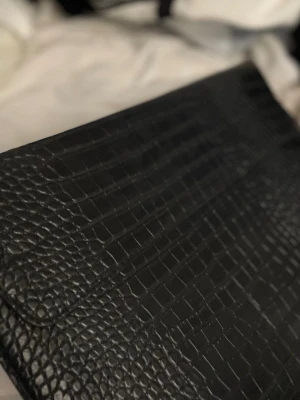 Svart kuvertväska från Celestio -  svart kuvertväska från Celestio i croco-mönstrat skinn. Väskan har en elegant och modern look med präglad yta som ger en lyxig känsla. 