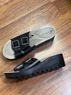 Svarta platåsandaler med spännen - Säljer ett par svarta sandaler från Lotus med två breda remmar och stora metallspännen. Sandalerna har en rejäl platåsula i syntet och mönstrad innersula för extra komfort. Perfekta för dig som gillar chunky stil och vill ha något som sticker ut.