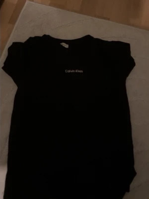 Svart t-shirt från Calvin Klein - Snygg svart t-shirt från Calvin Klein med klassisk logga tryckt på bröstet. Enkel och stilren design med rund hals och korta ärmar. Perfekt basplagg till garderoben.