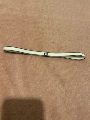 Vit elastisk hårsnodd Under Armour - Säljer en vit elastisk hårsnodd från Under Armour med svart logga. Perfekt för att hålla håret på plats under träning eller vardag. Enkel och stilren design.