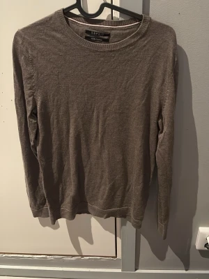 Brun merinotröja från Esprit - Säljer en stilren brun tröja från Esprit i 100% merinoull. Tröjan har rund halsringning, ribbade muddar och lång ärm. Perfekt för dig som gillar klassisk och enkel stil med skön känsla. Sitter som S/xs, passar perfekt till våren.