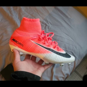 Nike Mercurial superfly V FG - Nike Mercurial fotbollsskor med högt skaft i röd och vit färg, svart swoosh och snörning. Skorna har stickad Flyknit-överdel och ACC-teknologi för bästa bollkontroll. Perfekta för dig som vill sticka ut på planen.