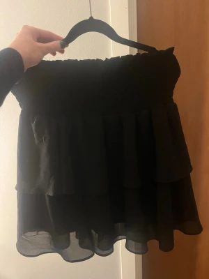 Svart volangkjol med resårmidja - Supersöt svart kortkjol med dubbla volanger och bred resår i midjan. Kjolen är gjord i ett tunt och lätt material, perfekt till somnaren. Den har en liten fläck som jag ej vet om den går att få bort (se bild)🩷🩷