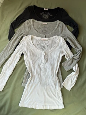  långärmade toppar från Marwin olik färg - Säljer  långärmade toppar från Marwin i svart, grått och vitt. Alla har rund halsringning, ribbad struktur och knappar framtill. Perfekta att styla eller bära som de är. Diskret logga.