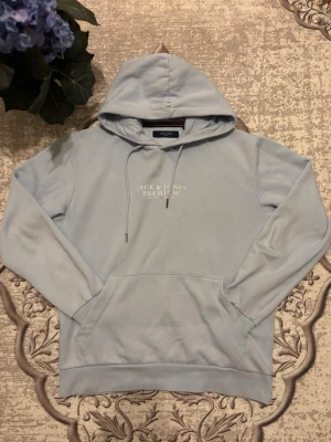 Jack & Jones premium Hoodie  - Snygg ljusblå hoodie från Jack & Jones Premium med broderad logga på bröstet. Klassisk känguruficka, dragsko i huvan och mjukt fleecefoder på insidan. Perfekt för chill dagar och enkel att matcha med jeans eller joggers. Man märker inte de efter man har kommit nära. Köpt den för 549! 