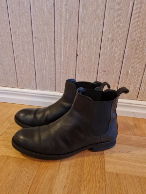 Svarta chelsea boots strl 41 - Klassiska svarta chelsea boots med elastiska paneler på sidorna och dragflikar bak. Rund tå och robust sula som ger bra grepp. 